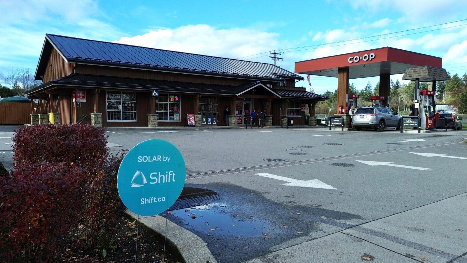 A photo of a business with BIPV (Building Integrated Photovoltaics) as the roof. A solar panel roof. Also, a lawn sign saying Shift. In Salt Spring, BC