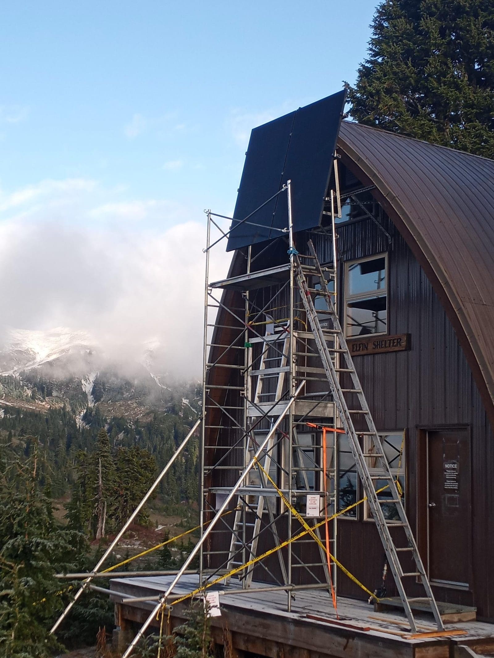 Image of an off-grid ranger station in the mountains of BC and black solar panels. As well as scaffolding