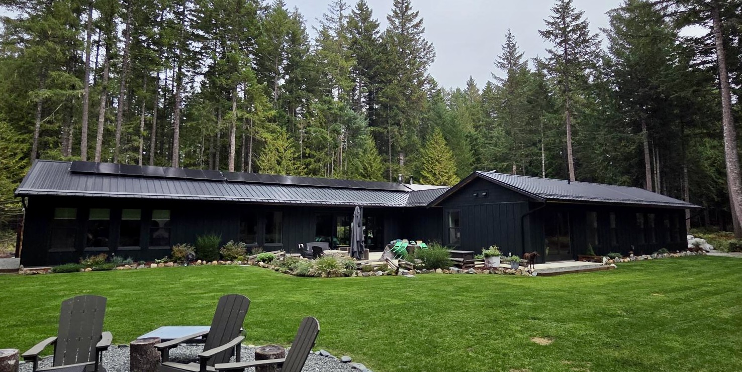 View from the backyard of a modern, rural off-grid home with solar panels on the roof.