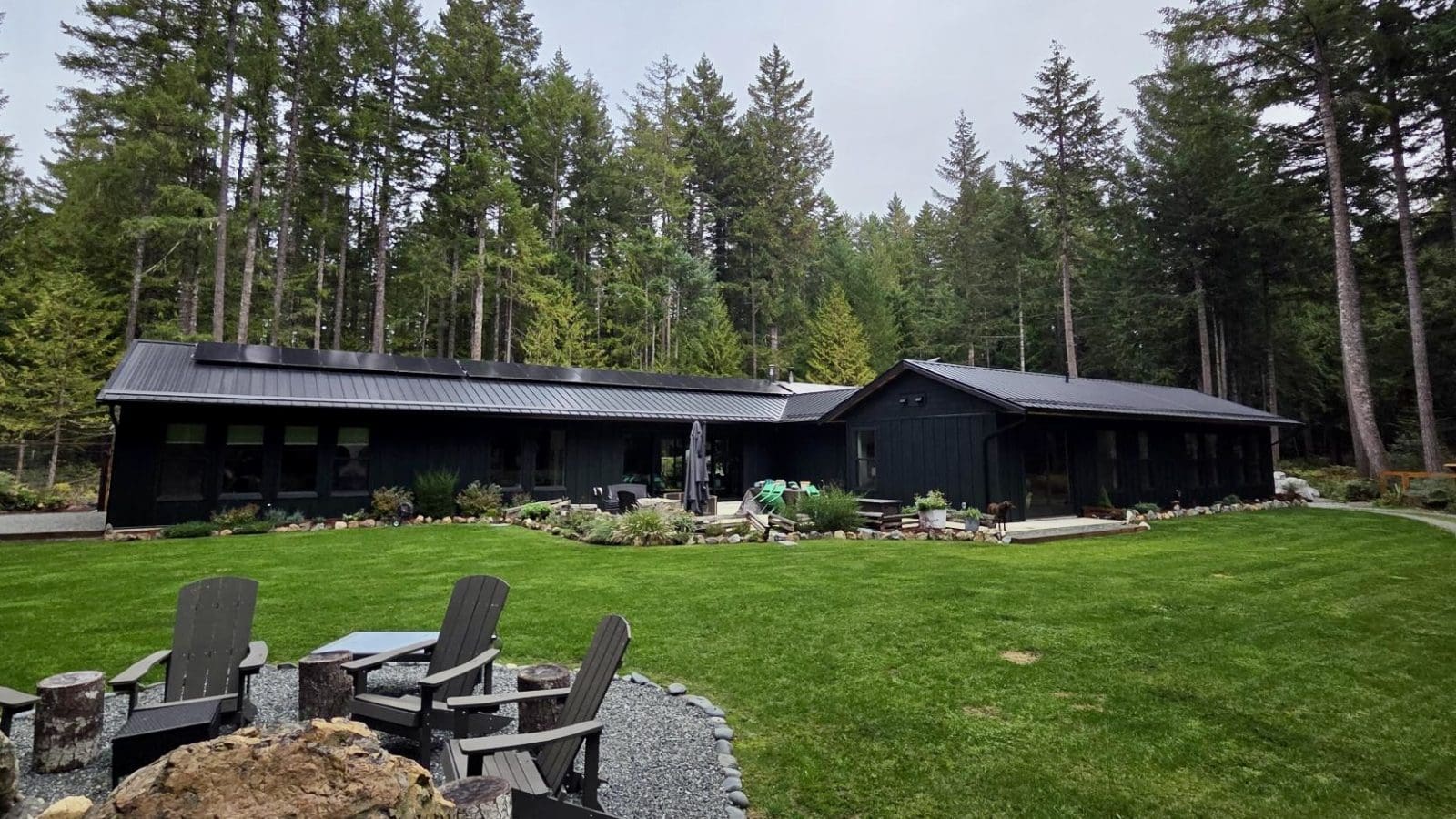 View from the backyard of a modern, rural off-grid home with solar panels on the roof.