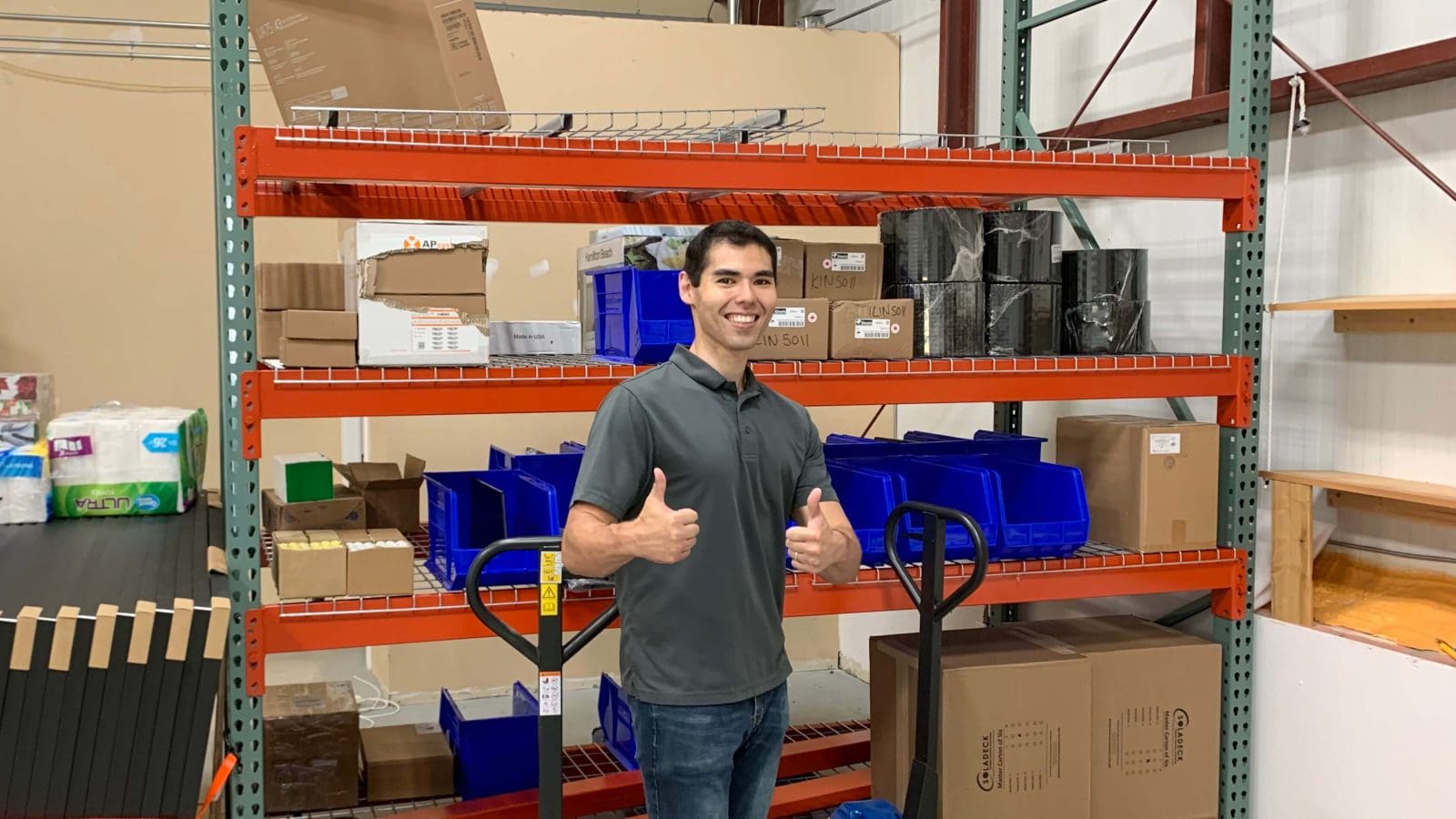 Team member standing in a warehouse, giving a thumbs up.