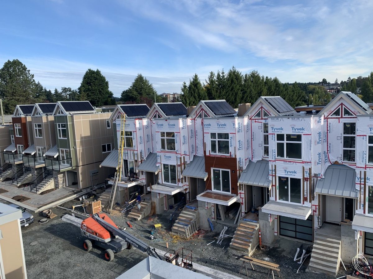 a head-on view of a series of townhomes with solar panels installed on all the dormers on each roof.